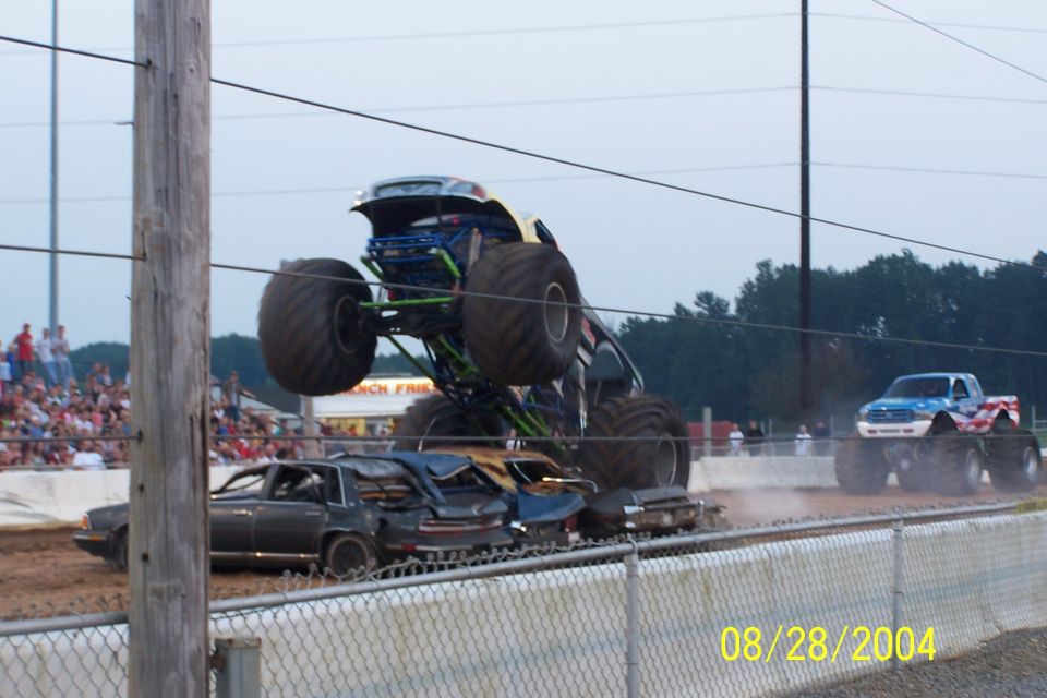 Monster truck mid-air over crushed cars, another monster truck in background