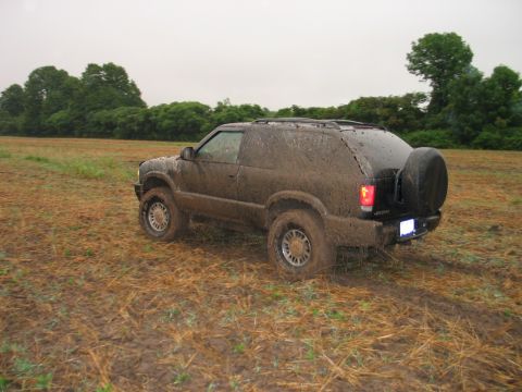 1995 Ford Bronco - A muddy black SUV navigates a wet, grassy field under an overcast sky.