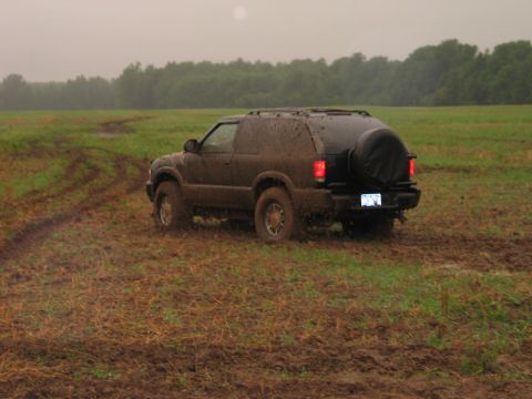 1995 Ford Bronco - A dark SUV is stuck in a muddy field, with tire tracks visible in the grass.