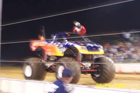 1979 Ford Bronco II - A monster truck with a patriotic paint scheme is captured in action, its massive tires visible as it moves across the dirt track.