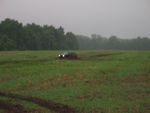 1995 Ford Bronco - SUV driving through a muddy field on an overcast day.