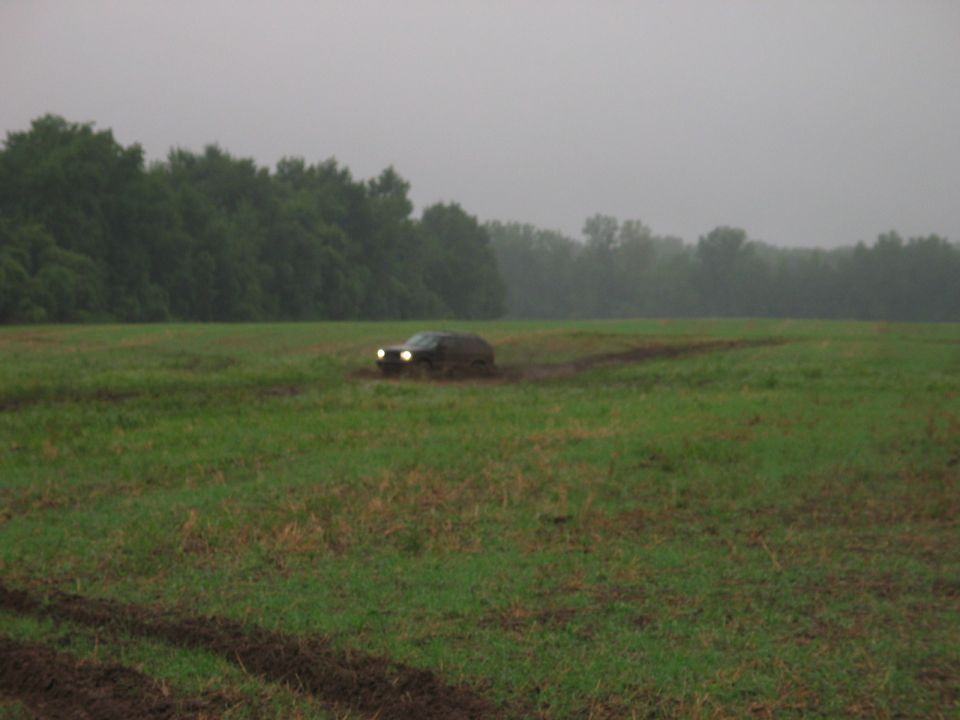 SUV driving through muddy field with trees in background