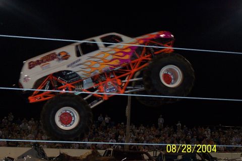 1979 Ford Bronco II - A monster truck performs a jump, suspended in the air against a dark background with a crowd watching below.