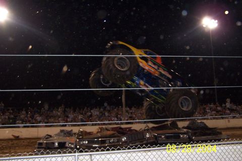 1979 Ford Bronco II - Monster truck performs a jump over wrecked cars during an event at night.
