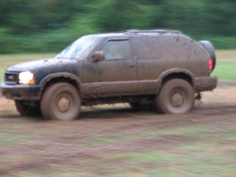 1995 Ford Bronco - This GMC SUV is covered in mud as it drives through a grassy field.