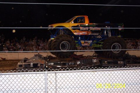 1979 Ford Bronco II - A monster truck drives over crushed cars in front of a crowd.