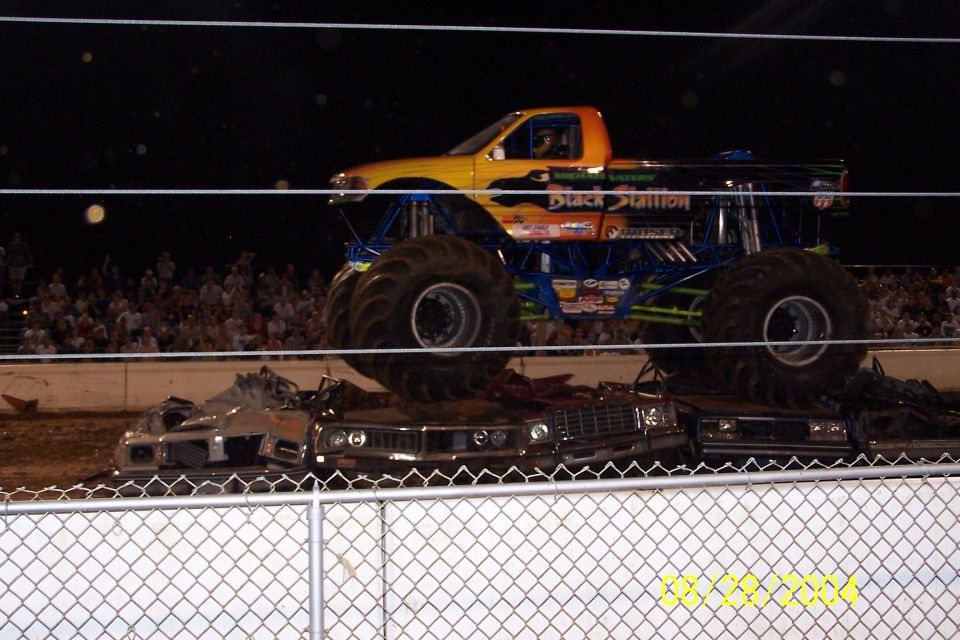 Monster truck with "Black Stallion" text crushing cars