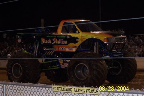 1979 Ford Bronco II - A monster truck with custom paint and sponsorship decals is parked on a dirt track.