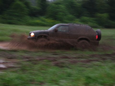 1995 Ford Bronco - An SUV navigates a muddy terrain, kicking up dirt as it moves through the mire.