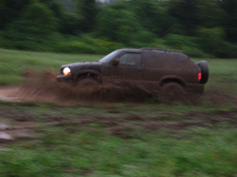 Mud-splattered SUV driving through mud, side view. Spare tire mounted on rear