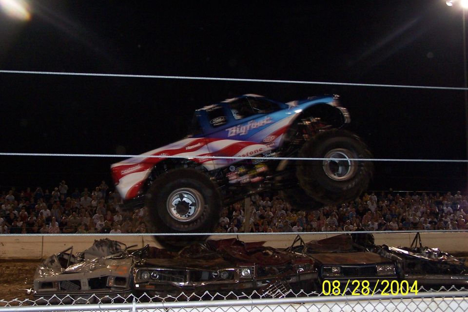 Bigfoot monster truck mid-air over crushed cars, crowd in background. Date stamp 08/28/2004