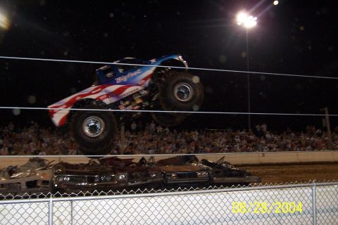 1979 Ford Bronco II - A Bigfoot monster truck performs a jump over several crushed cars during an event at night.