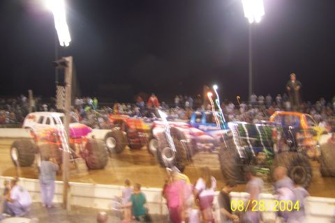 1979 Ford Bronco II - Monster trucks compete at a nighttime event with spectators in the background.