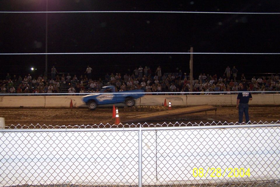Blue pickup truck racing on dirt track with crowd in background