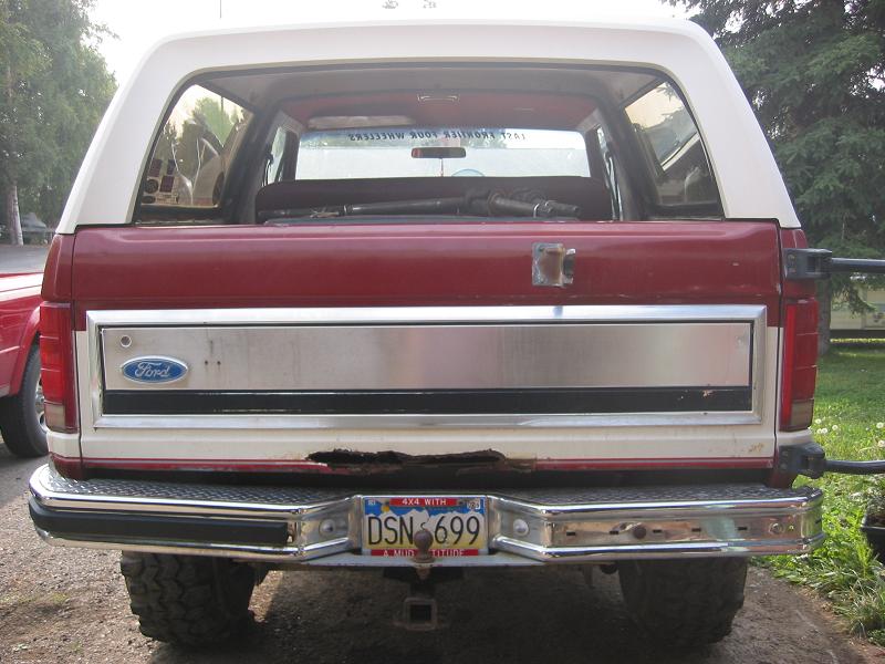 Rear tailgate of a red and white 1990s Ford Bronco with chrome trim and Alaska DSN699 plate