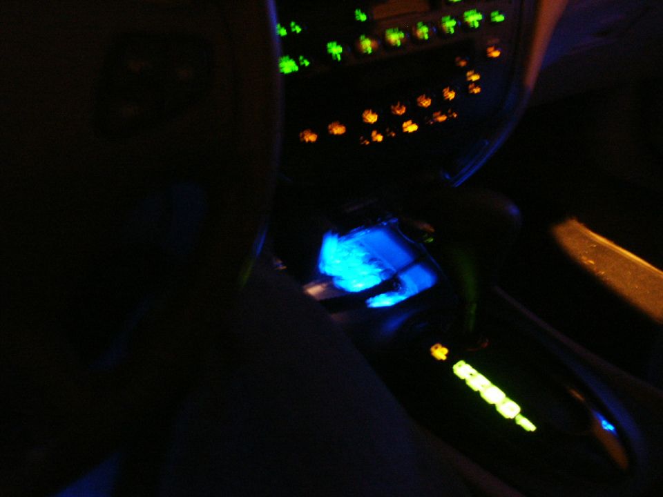 Dark car interior at night with green and amber dash buttons and blue-lit automatic shifter console