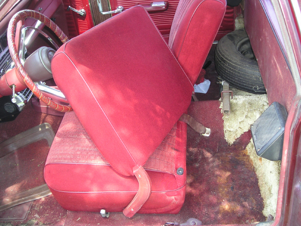 Folded red front bench seat tipped forward, spare tire and worn carpet behind it