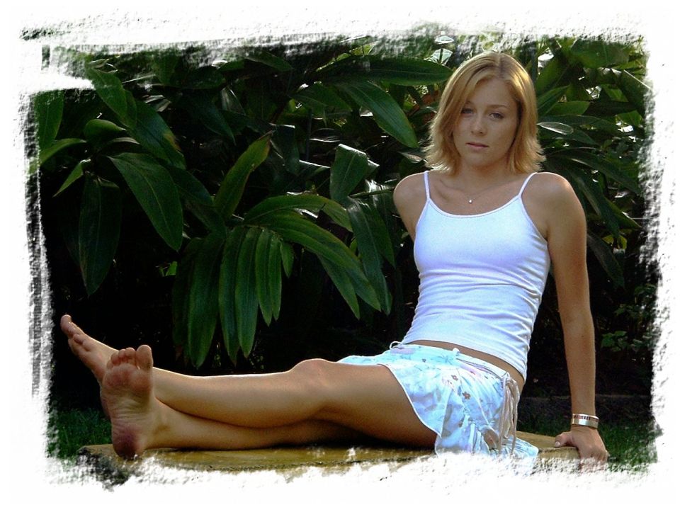 Woman in white tank top sitting outdoors in front of tropical plants