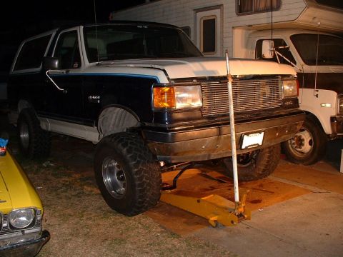 1990 Ford Bronco - A lifted 1990 Ford Bronco is shown with a yellow jack supporting its front end.