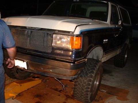 1990 Ford Bronco - A person works on a 1990 Ford Bronco, which is raised on a jack with its hood open.
