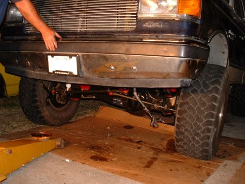 1990 Ford Bronco - A dark blue 1990 Ford Bronco's front suspension and bumper are visible, with a jack positioned to lift the vehicle.