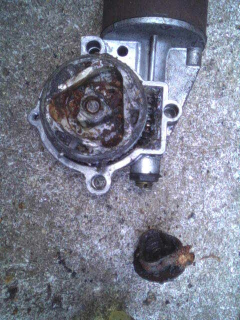 1987 Lincoln Town Car - A heavily corroded starter motor component lies on a textured concrete surface.