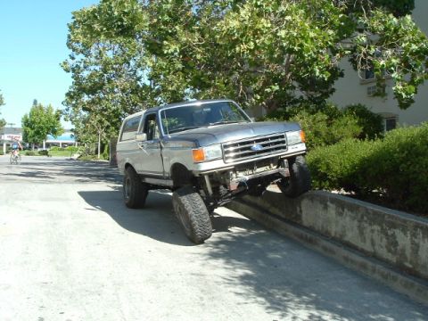 1989 Ford Bronco - This lifted SUV is shown testing its suspension by driving on a concrete barrier. The grille suggests a 1987 model year.