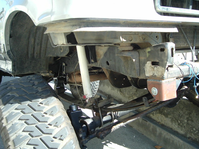 Underside of lifted Ford Bronco showing front suspension, shock, frame and mud tire
