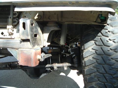 1989 Ford Bronco - This image shows the front suspension and a large tire of a modified off-road vehicle, with visible text from Supermotors.net.