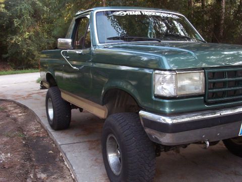 1989 Ford Bronco - This lifted green pickup truck has a two-tone lower body trim and chrome bumper details.