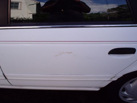 1998 Ford Taurus - Side view of a white car door with a visible rust spot and a black door handle.