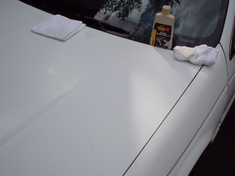 1998 Ford Taurus - A bottle of swirl remover and cleaning towels rest on the hood of a white car.