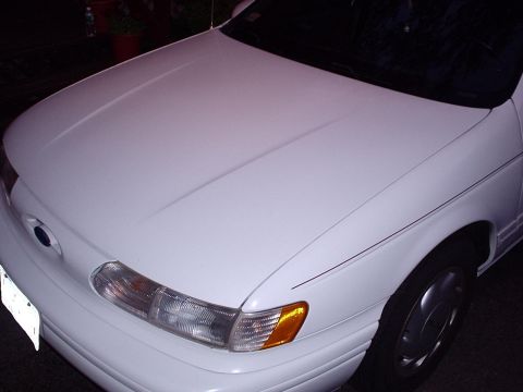 1998 Ford Taurus - Night flash shot looking down the hood of a white Ford sedan of the earlier squared-oval generation, showing the blue-oval nose badge, wrap…