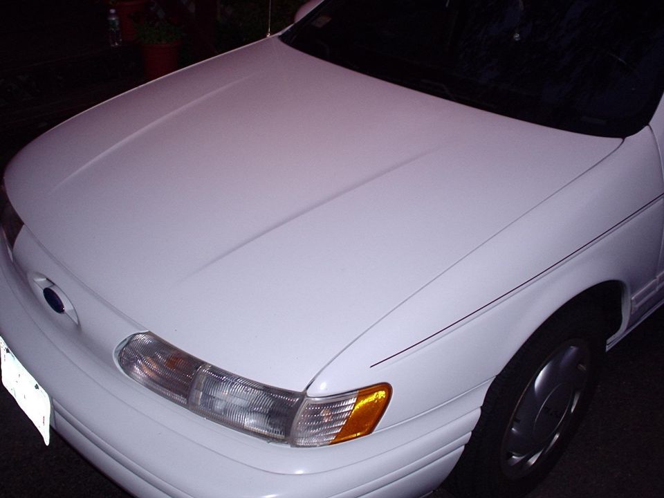 White Ford sedan hood and headlight at night with blue-oval nose badge