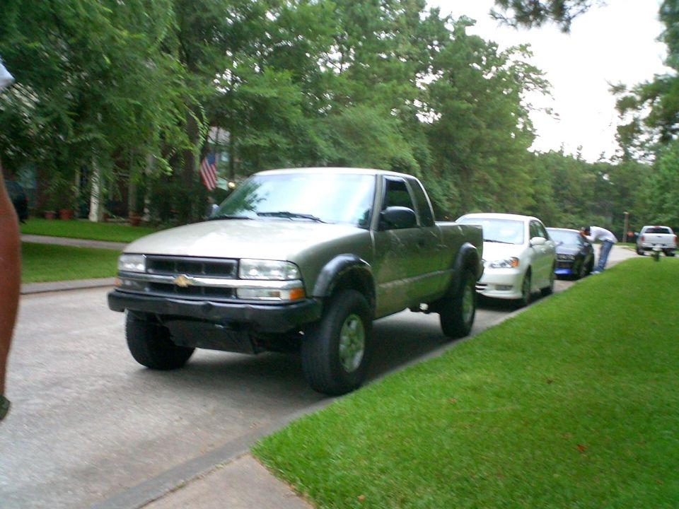 Lifted olive Chevrolet S-10 extended-cab pickup on a suburban street, cars lined up behind