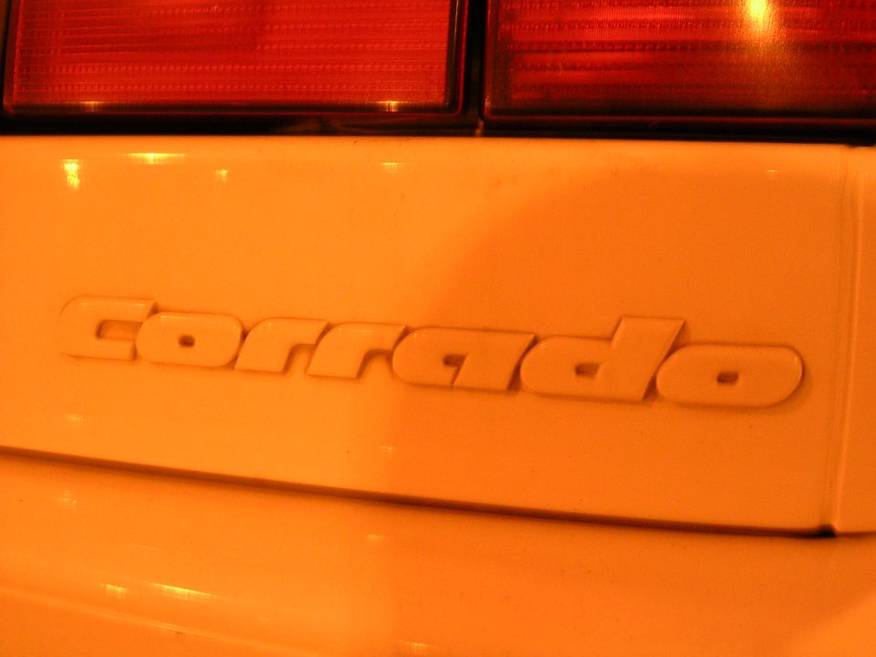 Close-up of a body-colored Corrado badge below red tail lights at night