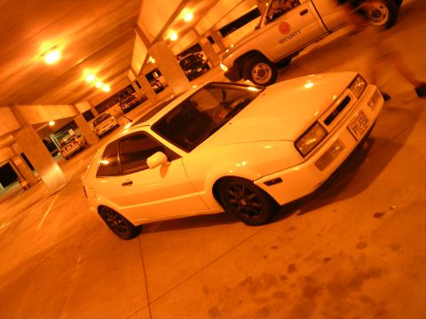 1990 Volkswagen Corrado - A white 1990 Volkswagen Corrado is parked in a dimly lit parking garage, with a security truck visible in the background.