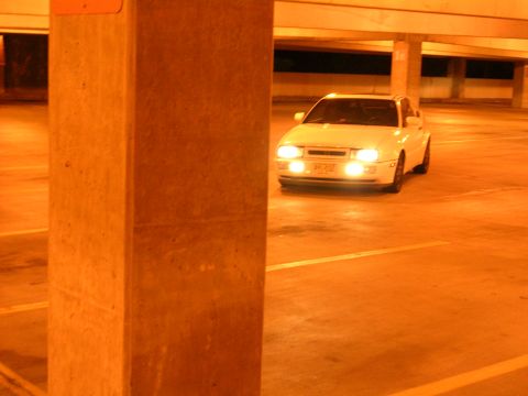 1990 Volkswagen Corrado - A white 1990 Volkswagen Corrado is parked in a dimly lit parking garage, its headlights illuminating the concrete surroundings.