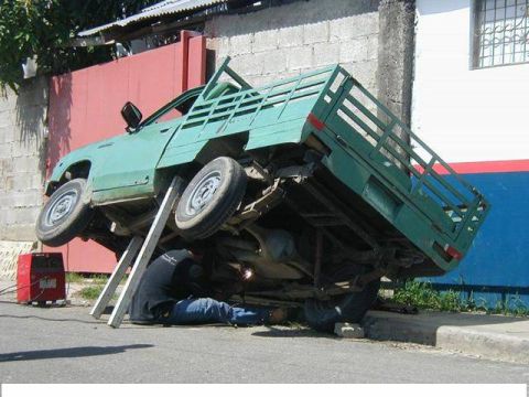 1994 Ford Bronco - A mechanic works on a green pickup truck that is precariously tilted on metal supports.