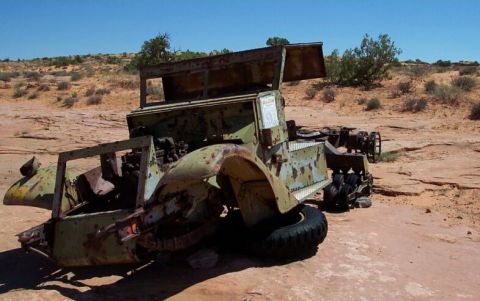 1990 Ford Bronco - This heavily rusted vehicle chassis sits abandoned in a dry, desert environment under a clear blue sky.
