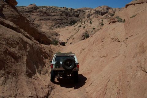 1990 Ford Bronco - A white 1990 Ford Bronco navigates a narrow, rocky canyon trail with another vehicle visible in the distance.