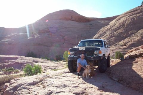 1990 Ford Bronco - A man and his dogs take a break with their off-road vehicle in a rocky, desert environment.