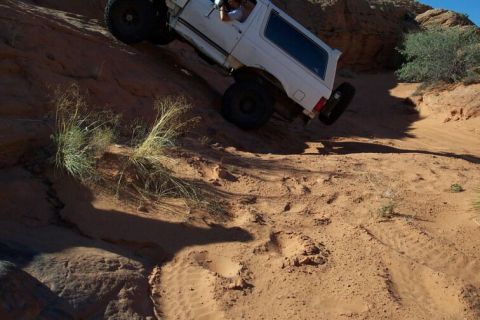 1990 Ford Bronco - White SUV navigates a challenging off-road trail with steep sandy slopes.