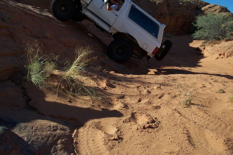 White SUV with off-road tires climbing a steep, sandy incline