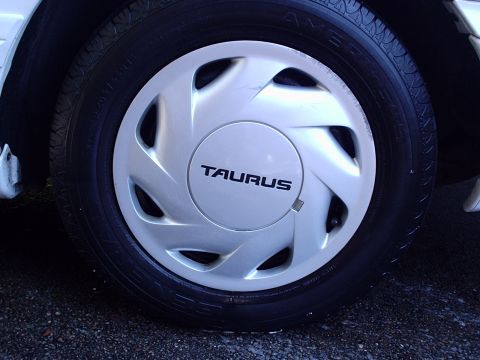 1998 Ford Taurus - The wheel cover clearly displays the 'TAURUS' name, indicating it belongs to a Ford Taurus.