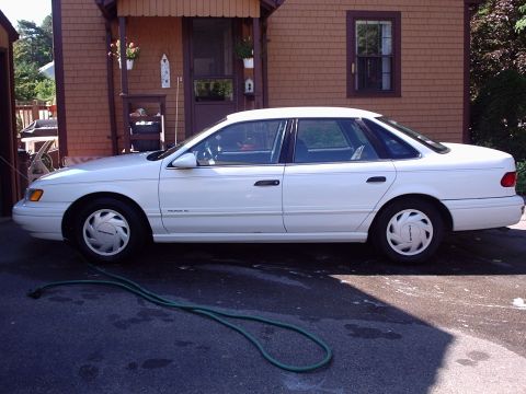 1998 Ford Taurus - A white sedan is parked on an asphalt driveway in front of a house.