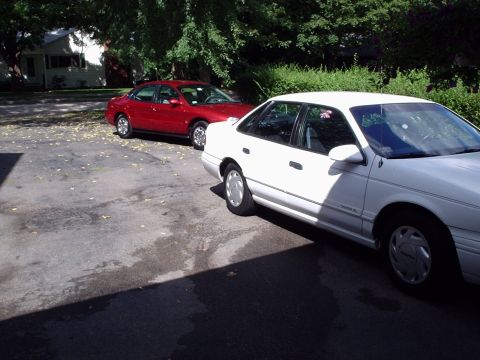 1998 Ford Taurus - A white sedan is parked in the foreground, with a red sedan visible behind it.
