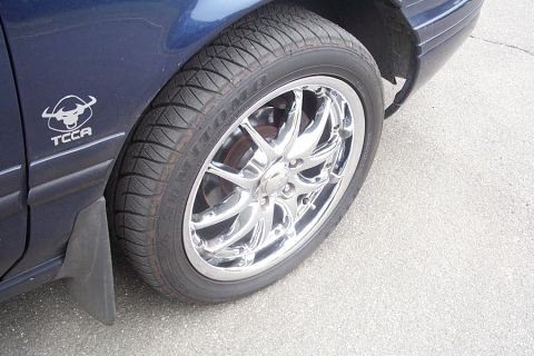 1993 Ford Taurus - A close-up of a car's fender and wheel shows a custom emblem and aftermarket chrome rims.