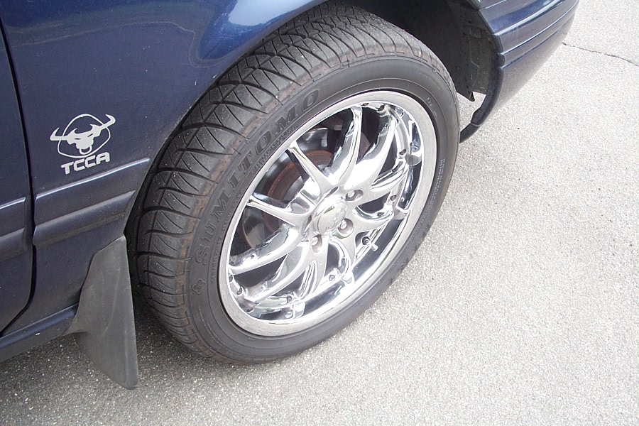 Dark blue car fender with a TCCA bull emblem and a chrome wheel with a tire
