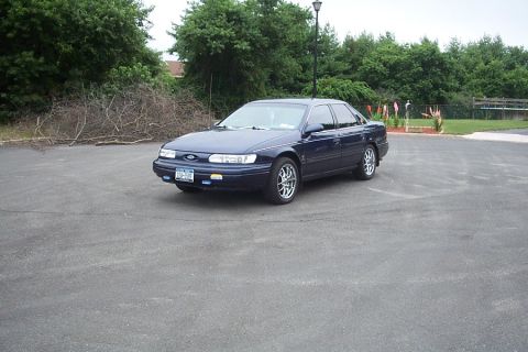 1993 Ford Taurus - A 1993 Ford Taurus sedan is seen from a three-quarter front view, parked on an asphalt surface with trees in the background.